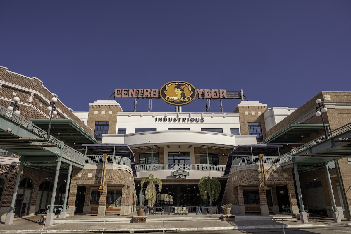 Front entrance of Centro Ybor with the large "CENTRO YBOR" sign above a brick building under a clear blue sky. This entertainment district is a popular landmark surrounded by restaurants, shops, and nightlife.