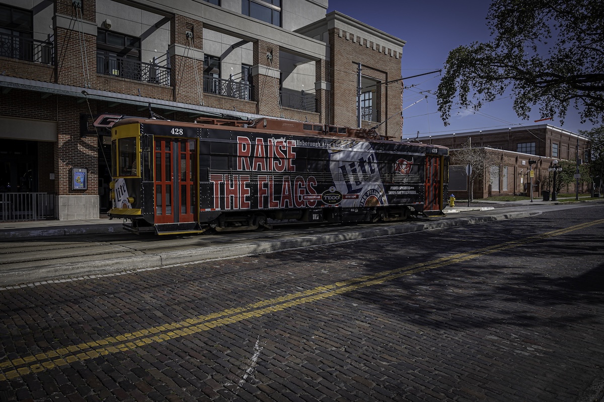 Historic TECO Line Streetcar stopped on brick-lined tracks in Ybor City with brick buildings and blue skies overhead. The streetcar provides an easy way to travel between Ybor City, Channelside, and downtown Tampa.