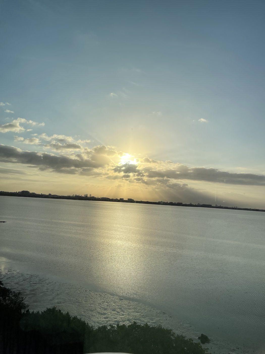 Golden sunset breaking through clouds over calm water with the distant Tampa skyline on the horizon. The peaceful waterfront view showcases one of the city's most romantic settings for an evening together.