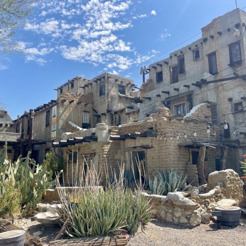 An adobe-style multi-level building with wooden beams, desert plants, and string lights is part of Cabot’s Pueblo Museum, showcasing Native-inspired architecture. Touring this historic handmade homestead is one of the most unique things to do in Desert Hot Springs.